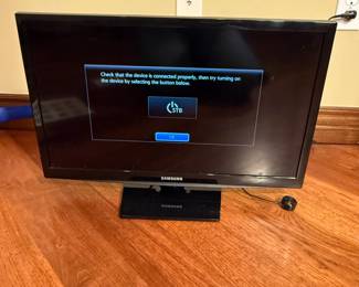 Samsung brand monitor, 24 inches in size, black color, LCD display. Features on-screen text indicating device connection issues. Model number LT24H310, with a sleek design and a base stand. Includes an HDMI port for connectivity. The back has a label detailing specifications including model and energy certification.