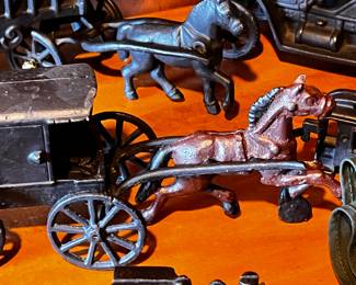 Cast Iron Toys: Several cast iron vehicles, including a circus wagon, cars, a horse-drawn carriage, and a train engine