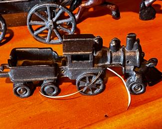 Cast Iron Toys: Several cast iron vehicles, including a circus wagon, cars, a horse-drawn carriage, and a train engine