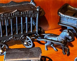 Cast Iron Toys: Several cast iron vehicles, including a circus wagon, cars, a horse-drawn carriage, and a train engine