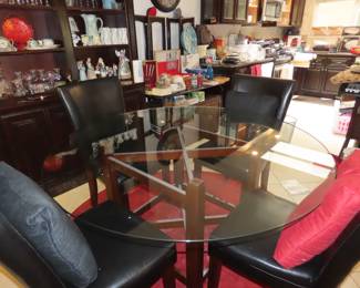 Round glass dining table with four black leather like chairs.
