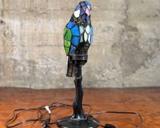 This lot features a Tiffany style stained glass parrot lamp. No fitted bulb, but tested with other bulb and works as it should. The stained glass parrot also appears to be in excellent condition. This lamp measures, 16” H x 5” W x 5” D.