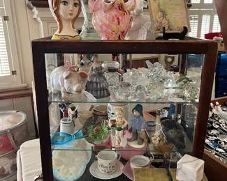 This showcase contains, vintage Japan piggy banks, porcelain figures, Antique opalescent drapery  tie backs from New England circa 1800's, Victorian cranberry glass, vintage splatter confetti art glass, paper weights