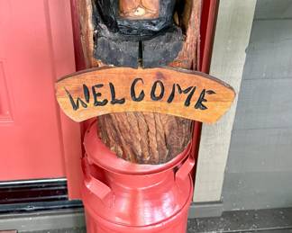 Carved wood bear welcome sign on painted metal milk can