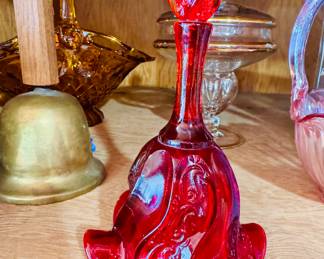 : Deep ruby red pressed glass bell with a flame-shaped handle and ornate swirl patterns on the skirt. Victorian-style design, likely 1970s–1980s reproduction.