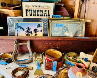  Includes a painted wolf pottery vase, silverplate tray, Western-style belts, brass steer-head wall hook, horse tack, framed art, and a “Notice Funeral” novelty sign.