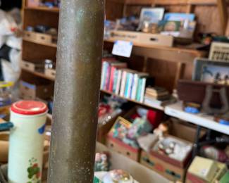 Tall brass artillery shell casing, likely WWII or post-war era. Cylindrical with flared base rim. Heavy patina and some oxidation present, indicating age.