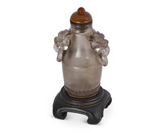 2146
A Chinese smoky rock crystal snuff bottle
19th century
The urn-form bottle with opposed dragon mask handles with rings, mounted on a carved wood stand
Overall: 3.625" H
Estimate: $400 - $600