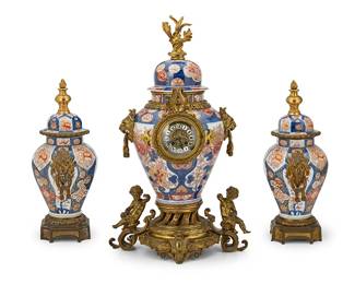 2264
An Imari-style porcelain and bronze three-piece clock garniture
19th century
Movement marked: CB / 158
Each lidded porcelain vase decorated with red and blue floral and avian motifs, mounted with Continental bronze adornments including opposed lion's head ringed masks and a flame finial, the central vase housing a two-train movement clock with Roman numeral enameled metal hour track, additionally adorned with bronze griffins and putti and mounted on an elaborate pierced base
3 pieces
Clock with lid: 29" H x 17.5" W x 13" D; Each garniture with lid: 19.25" H x 10.25" W x 7.625" D
Estimate: $2,000 - $3,000