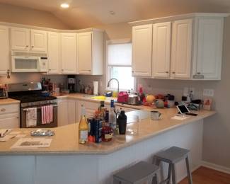 Crisp white C-shaped kitchen; two bar stools