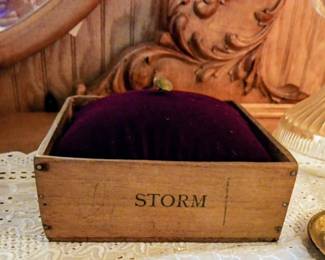 Antique wooden box with the word "STORM" printed on it, containing a purple velvet cushion