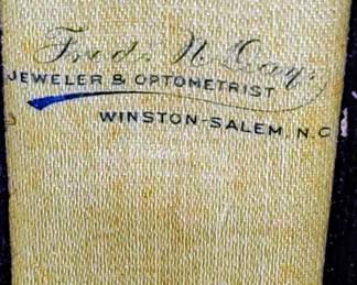 The purple velvet box clearly states the dual professions of "JEWELER & OPTOMETRIST". 
The location is specified as "WINSTON-SALEM, N.C" this was common in the early 1900s to have two businesses in one. 