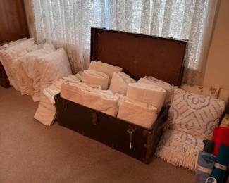 Lots of mattress pads twin and full with vintage bedspread, old trunk and pillows