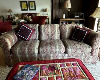 Upholstered couch in burgundy and green. Wooden side tables, lamps, book case, dvds, audiobooks on tape