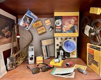 1950's: Bakelite Kodak Brownie Hawkeye Camera, +
Bell & Howell Two Fifty Two 8mm Film Movie Camera Camcorder, Kodak Sound Recording Tape, Sunglasses, Buddy Metal Pocket-Size Hand Warmer, Fishing Themed-Print & Fish Net, etc.