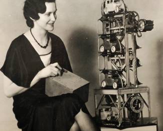 PRESS PHOTOGRAPH OF MODEL OF A CAR ELEVATOR USING ARCADE TOY CARS