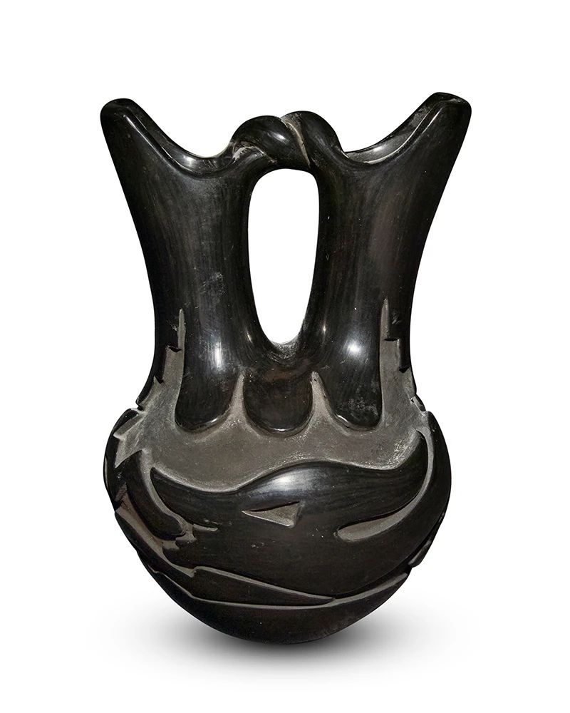 1
Reycita Cosen (1927-2012, Santa Clara Pueblo)
A blackware pottery wedding vase, 1989
Signed and dated to underside: Reycita Cosen / Santa Clara / 6-20-89
The stone-polished black vase featuring flared spouts joined by a twisted arched handle, with a deeply carved Avanyu water serpent motif to body
8.25" H x 5.625" Dia.
Estimate: $200 - $400