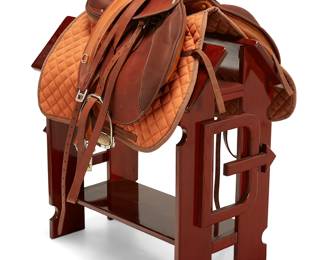 96
An Hermès Brasilia leather saddle and accessories
Mid/late 2000s, France
Stamped to underside: E. Hermès / 45 491 [serial number] / Made in France; stamped to leather straps: Hermès / Paris; stamped to stirrups: Hermès; pad with label: Hermès / Paris
The saddle custom-made of natural tanned full grain leather, with branded grommets, rounded and padded flap, rounded cantle, branded stirrups and contoured orange quilted fabric pad, 16" seat, girth belt (125cm), four fixed martingale bridle leather straps, and two original Hermès dust bags and a saddle cover, together with a wood saddle stand bearing the D Arrow brand
Seat: 16"; Gullet width: 3.5"; Flaps: 13.5" H; Stand: 31" H x 18" W x 30" D
Estimate: $2,000 - $3,000