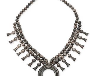 54
A Southwest sterling silver squash blossom necklace
Early/mid-20th century
Unmarked
Comprising a silver three-wire naja with fourteen blossoms, all suspended from a double strand of silver ball beads
29.5" L x 3" H
251.7 grams
Estimate: $1,000 - $1,500