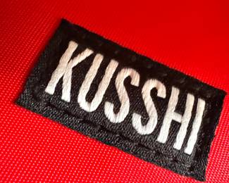 KUSSHI Logo Detail – Premium Makeup and Travel Bag Brand Tag on Red Fabric