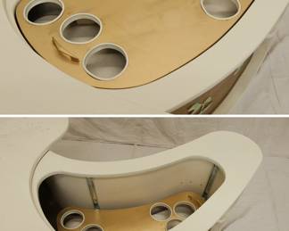 Another view of the "Grand Server" mid-century modern boomerang/kidney shaped coffee table with collapsible bar cabinet, manufactured by A.H. Stock Manufacturing Company. This design was showcased at the 1964 World’s Fair in New York City as an example of American modern furniture. With two external shelves, locking side cabinet doors and resting on legs with casters, this table’s white laminate top swings open to reveal an inside compartment with a mechanical tray: just pull up on the brass handles which lock the tray into place at table height. Wrapped with textured gold vinyl on the sides, with applied mother of pearl pieces in Asian decorative motif.