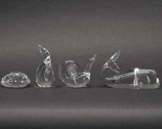 Steuben Glass Whale, Turtle, Penguin, and Snail figurines. A group of four sparkling clear Steuben glass figurines and hand coolers, comprised of Turtle Hand Cooler (shape No. 5514) and a Whale figurine (shape No. 8075) both designed by Lloyd Atkins, a Snail (shape No. 7982) designed by David Hills, and Adult Penguin figurine. Each marked Steuben on the base. Measurements: Whale 5-1/2 inches L x 3-1/2 inches H, Turtle 2-1/2 inches L x 1 inches H, Snail 3 inches L x 3 inches H, Penguin 2 inches L x 3-3/4 inches H.