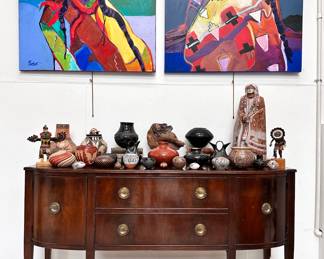 A beautiful Federal style sideboard graced with a collection of Native American art including pottery from Santa Clara Pueblo, Acoma Pueblo, and Jemez Pueblo artists Marcella Yepa, Mary Rose Toya, Sharon Lewis, Darin Victorino, Madeline Naranjo, Tina Garcia, Jackie Shutiva; Mata Ortiz pottery, Hopi Kachina dolls, and more, all beneath two vivid original paintings of Native Americans in traditional dress by renowned artist Malcolm Furlow, an award-winning painter, whose accolades include the Silver award from the Sorbonne, and the highly coveted Gold Award from the world-renown Luxembourg Museum, Paris.
