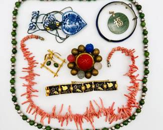 An assortment of Asian jewelry items including carved jade on intricately knotted cord, a green jade and silver metal bead necklace, a blue-and-white ceramic bead necklace on knotted blue cord, a delicate branch coral necklace, a green jade and silver vermeil pendant, a gold-tone brooch faux bamboo brooch embellished with jade, a carved stone bead brooch with a cinnabar centerpiece, a damascene link bracelet, a Siam silver enamel bracelet and hinged bangle.