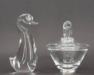 Designed by Irene Benton and introduced in 1943, this Steuben Glass Ram’s Head Candy Dish, shape No. 7936, has five separate bits composing the ram’s head atop the lid. Signed Steuben on the base, measuring 5 inches W x 6 1/2 inches H. The Upright Duckling figurine, shape No. 8129, designed by Lloyd Atkins and introduced in the 1960s, measures 3 1/2 inches L x 2 inches W x 7 1/2 inches H and is hand-signed Steuben on the base.