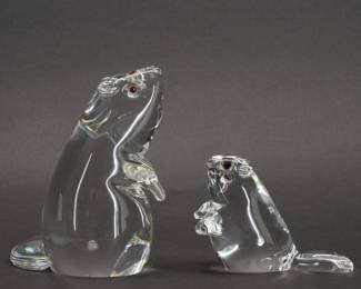 Pair of Steuben Glass Beaver Figurines with Garnet Eyes. A sparkling pair of Steuben clear glass beaver figurines with inset garnet eyes. From a 1975 design by Lloyd Atkins. Both pieces hand signed Steuben on the base. Beaver Upright shape No. 8307 is 5 inches L x 5 inches W x 6 inches H, Beaver Small Upright shape No. 8360 is 5-1/4 inches L x 2-1/2 inches W x 3 inches H.