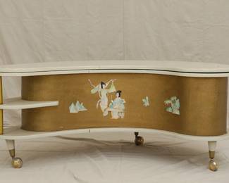 Portable and retro - The "Grand Server" mid-century modern boomerang/kidney shaped coffee table with collapsible bar cabinet, manufactured by A.H. Stock Manufacturing Company. This design was showcased at the 1964 World’s Fair in New York City as an example of American modern furniture. With two external shelves, locking side cabinet doors and resting on legs with casters, this table’s white laminate top swings open to reveal an inside compartment with a mechanical tray: just pull up on the brass handles which lock the tray into place at table height. Wrapped with textured gold vinyl on the sides, with applied mother of pearl pieces in Asian decorative motif.