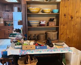 The top shelf features several Pryrex mixing bowls. The middle shelf holds a large striped mixing bowl, a ruffled class bowl/vase, and a vintage coffee grinder. The bottom shelf offers claw-foot candle holders and two 