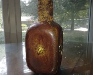 Leather decanter with gold lion detailing, cork with wood circle stopper, and braided neck wrapping.