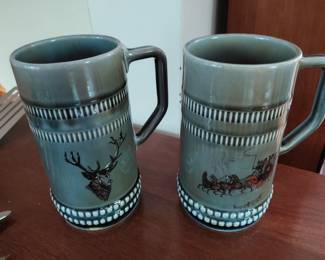 Pair of green colored pottery steins with deer and sled detail.