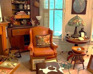 Upholstered arm chair, cowhide footstool, round oak table, Tiffany lamp, western art and corner cabinet.