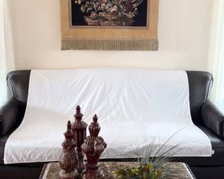 Fringed wall tapestry featuring a floral motif. Includes hanging rod, which must be removed from wall at pick up. Bring tools and step stool. H 37" x W 44". A trio of burgundy ceramic accents ranging in size from H 15" to H 17". Wooden wall sconce filled with a faux floral display, H 32". Sofa not included.