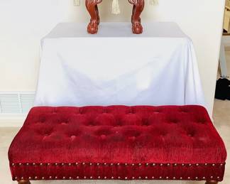 Burgundy tufted settee with rivet accents, H 17" x W 39" x D 19". Some wear on the seat fabric. One leg is loose. Upholstered footstool featuring decorative tassels and wood carved legs, H 12" x 17" diameter. Both items made in china.