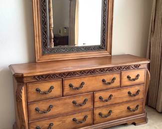 Wood dresser and mirror featuring an intricate design and metal accents. Matches lots 1 and 3. Dresser measures H 34" x W 66" x D 20". Mirror measures H 46" x W 42". Bring tools to remove mirror from dresser for transport. Minor nicks and scratches as well as water marks on surface. Receipt from consignor shows Ashley as the brand of furniture.