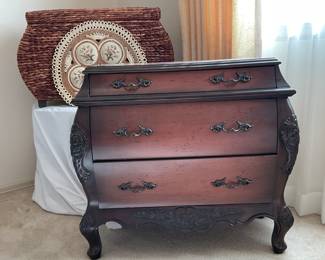 Wood veneer bombay style chest, no manufacturer found. H 29" x W 30" x D 16". Minor nicks and scratches. Rattan bombay style basket with lid, H 17" x W 29" x D 14". Some wear along the edge of the lid. Refer to photos.