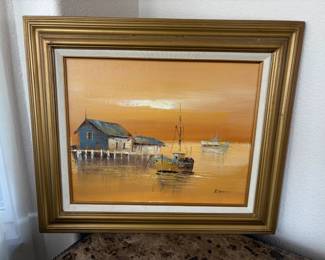 Appears to be an original oil painting depicting a coastal home and sailboat. Gold toned wood frame and linen mat. Artist name is not legible. H 24" x W 27".