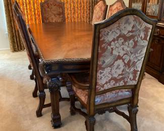 Ashley Classical designed wood veneer dining table featuring carved edges and (1) extension leaf. Table measures H 29" x W 88" x D 44" with leaf included. Leaf accounts for 18" of the width of the table. Additional leaf also included. Two (2) formal dining armchairs featuring a brown floral upholstered back and seat. Seats have protective plastic covering. H 47" x W 26" x D 21". Four (4) matching side chairs which measure H 47" x W 22" x D 20". Matches lot 102. Objects shown in background are NOT included. Receipt from consignor shows Ashley as the brand of furniture.