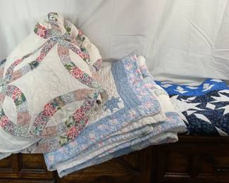 Three (3) unique quilts, one of which appears to be hand stitched. Starburst pattern appears to be hand stitched and fit a size king bed. Wedding ring pattern appears to fit a size queen. Blue quilt measures 66" square. Some tears and rips on all quilts except the blue.