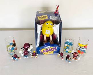 New M&M LA-Z-BOY dispenser, sealed in box. Set of (3) Smurfs collector's glasses, dated 1982. H 6" x 2 1/2" diameter. Set of (7) California raisin plastic figurines.