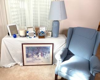 A variety of items featuring a blue wingback chair H 40" H x W 30" x D 27 1/2", a framed print titled "Promonading by Edward Clifford" H 24" x W 30", and a blue art deco style lamp (powers on H 33" x 18" in diameter. Also included are a variety of picture frames, large candle, small vase, and a glass enclosed flower. No manufacturer found on chair or lamp.