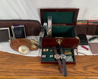 Seven (7) new men's wallets, many of which are made of leather. Men's two tone eagle belt buckle. Men's wood valet featuring a brass duck head. Wood jewelry box with key H 7" x W 12" x D 7". Additional items as shown in photos including cufflinks and more.