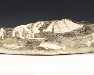 A 20th century Inuit carved Whale bone from the Pangnirtung hamlet, Qikiqtaaluk Region, Canada. Decorated with a carved relief genre scenes featuring hunters with seal and narwhal at front, and figures with igloo and polar bear on the reverse. Retains original "Canadian Eskimo Art" Igloo tag. Some cracks along length. Approx. 30 x 7 2/4" high overall. ESTIMATE $600-800