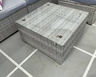Coffee table of grey woven outdoor material with glass top with corners tied in