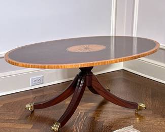 Councill Furniture "Keene" Oval Cocktail Table | Councill Furniture (Grand Rapids, Michigan) presents the "Keene" oval cocktail table, a mahogany table with satinwood border, tulipwood inlay along the tabletop sides and center, a central urn pedestal, and brass claw feet. - h. 18 x w. 44 x d. 27.25 in