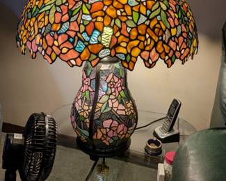 This is a magnificent and artistic table lamp in the iconic Tiffany style. The lampshade and the base are both crafted from beautiful, multi-colored stained glass in a stunning floral motif. The lamp features a unique dual-light function, allowing the top, the base, or both to be lit at once, creating a truly spectacular glow. This is a one-of-a-kind statement piece that will be the focal point of any room.
