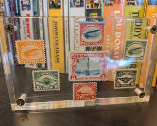 This is a beautiful and unique collection of vintage US Air Mail stamps from the 1920s and 1930s. Displayed in a clear acrylic frame, these stamps showcase a range of iconic designs, from biplanes and the Liberty Bell to the famous Rocky Mountain beacon. This piece is a perfect blend of American history and art, making it an excellent decorative accent for any space.